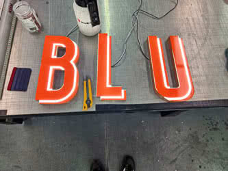 LED sign letters on a workbench, lit up, spelling out B L U