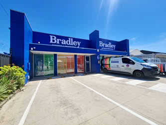 Front left view of a business and its parking lot, belonging to 'Bradley Trade Services', blue painted building, sunny day
