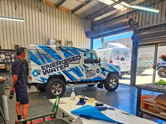 Custom business graphics wrap on a Landrover 110 vehicle, side view inside a workshop, belongs to Adelaide Pool Patrol Energized Water