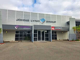 Front and slightly left view of a business building and parking lot, belonging to Johns Lyng Group, overcast day