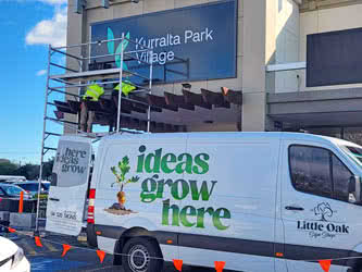 Workers on a scaffold installing a large sign onto a shopping centre building, outside on a sunny day