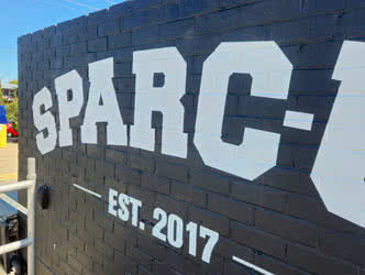 Cropped view of painted business signage lettering on a black-painted brick wall, front right view, clear sunny day