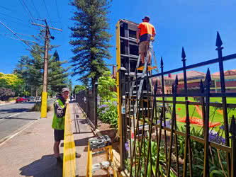 Workers installing a large pylon sign near a fence, outside on a sunny day