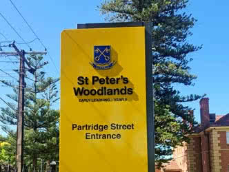 Cropped view of the top of a pylon sign belonging to 'St Peter's Woodlands', outside on a sunny day