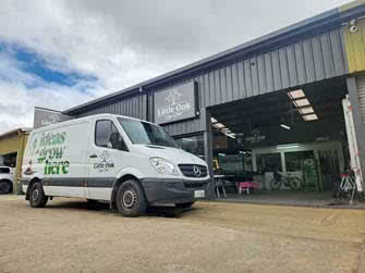 Front-right view of business and workshop with open roller door and work van parked in front of it
